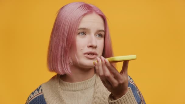 一个粉红头发的年轻女人用黄色智能手机和黄色背景说话 — 图库视频影像