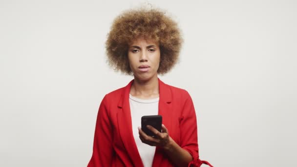 白い背景に設定されたスマートフォンでネガティブなメッセージを読み 感情でカメラを見ている女性 — ストック動画