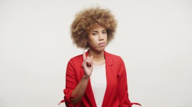 Kırmızı ceketli kadın beyaz arka planda tek bir parmak hareketiyle uyarı yapıyor.