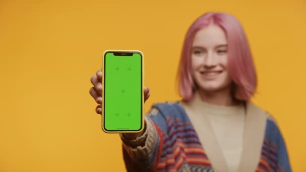 拥有明亮粉色头发的年轻人手持带有绿色屏幕的智能手机 准备好了应用或内容放置 — 图库视频影像
