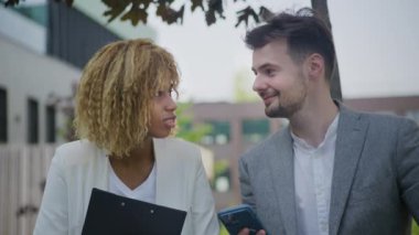 Açık havada erkek ve bayan bir iş arkadaşı arasında neşeli bir etkileşim, akıllı bir telefondan içeriği paylaşmak.