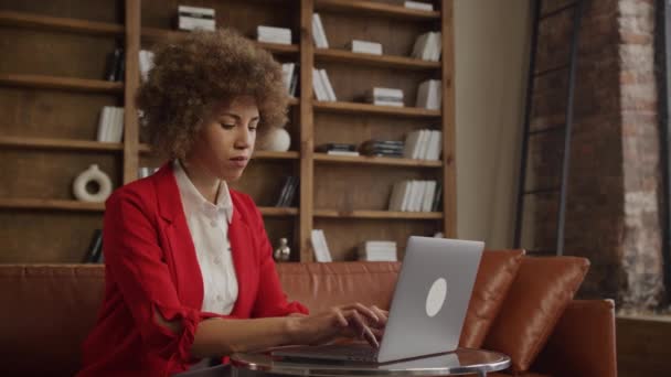 在阁楼式的客厅里 一位穿着充满活力的红色西装的创业者在笔记本电脑上专心致志地打字 — 图库视频影像