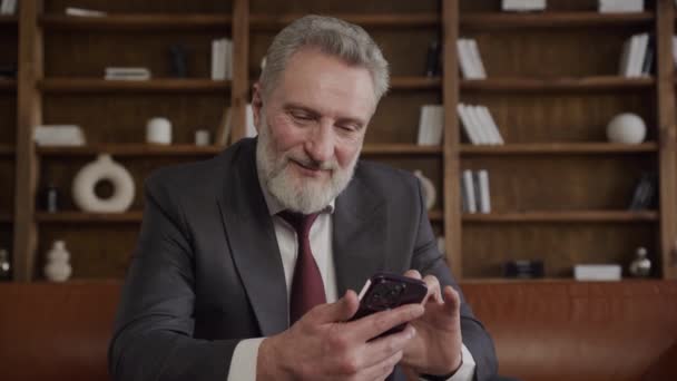 一位衣着优雅 留着胡子的资深商人笑着在时尚的办公室里使用智能手机 — 图库视频影像
