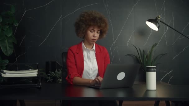 カーリーヘアスタイルの若いプロフェッショナルは 暗い大理石の背景を持つ現代のオフィスで彼女のラップトップに集中しています — ストック動画