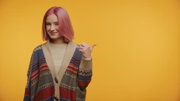 コピースペース カラフルなニットウェア 活気のある黄色の背景で親指を指すピンクの髪の若い女性 — ストック動画