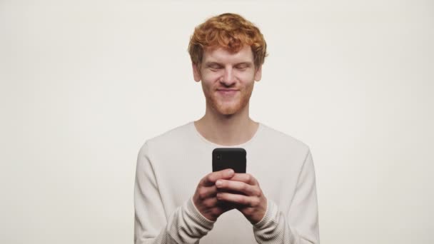 Homem Ruivo Sorrindo Enquanto Olha Para Seu Telefone Contra Fundo — Vídeo de Stock