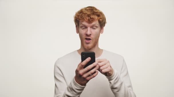 Rudowłosy Mężczyzna Pokazuje Zaskoczenie Podniecenie Podczas Oglądania Jego Smartfona Ekran — Wideo stockowe
