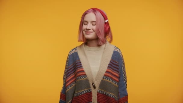 ピンクの髪とヘッドフォンの平和な若い女性は 黄色の背景に隔離された楽しみで目を閉じました — ストック動画