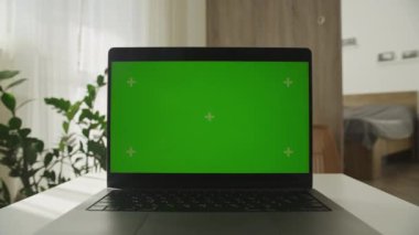 Dolly zoom, parlak bir ev ortamında masada yeşil ekranlı bir dizüstü bilgisayar aç