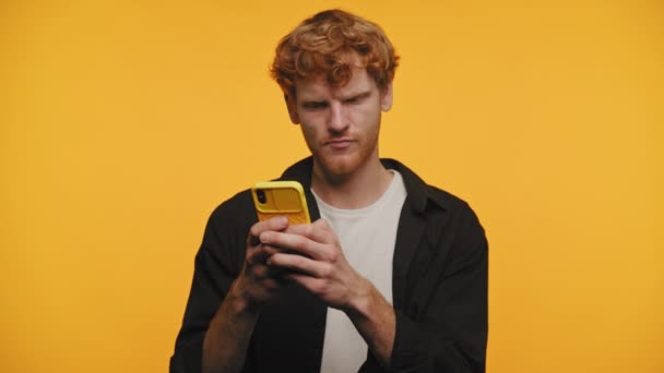 Gember Harige Man Glimlachend Terwijl Hij Sms Een Gele Smartphone — Stockvideo
