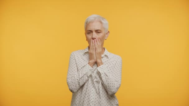年长的女人 满脸愁容 双手捂住嘴 背对着黄色的背景 — 图库视频影像