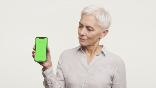Ώριμη Γυναίκα Που Παρουσιάζει Κινητό Τηλέφωνο Λευκή Πράσινη Οθόνη Κατάλληλο — Αρχείο Βίντεο