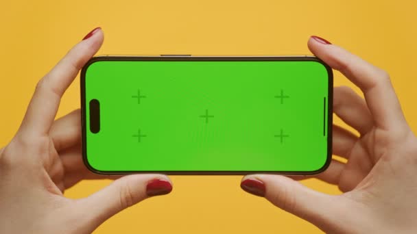 黄色い背景に緑色のスクリーンでスマートフォンを水平に保持する赤いネイルポリッシュで手からズームアウト — ストック動画