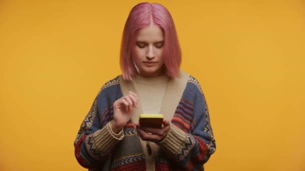 Młoda Kobieta Różowymi Włosami Wygląda Szokująco Trzymając Smartfona Żółtym Tle — Wideo stockowe