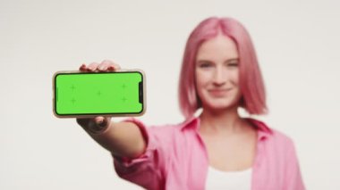 Pembe saçlı gülümseyen kadın elinde yeşil ekranlı akıllı bir telefonla içerik yerleştirmeye hazır bekliyor.