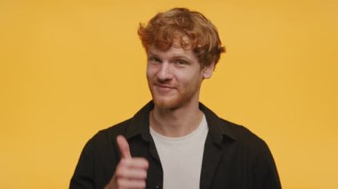 Kıvırcık saçlı, gülümseyen bir adam sarı arka planda siyah bir gömlek giyiyor.