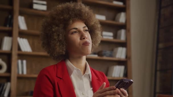 Zamyślona Bizneswoman Kręconymi Włosami Wyglądająca Troskliwie Trzymając Smartfona Biurze — Wideo stockowe