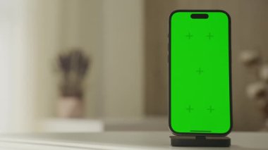 Birleşiklik için yeşil ekranlı bir akıllı telefon, solunda fotokopi alanı olan kablosuz şarj standında, yumuşak odaklı daire arka planına karşı durmaktadır.