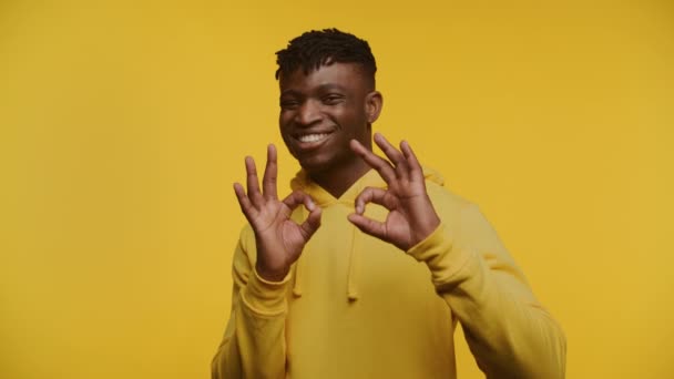 黄色のフーディーで陽気な男はOkのサインを与え 活気のある黄色の背景 — ストック動画