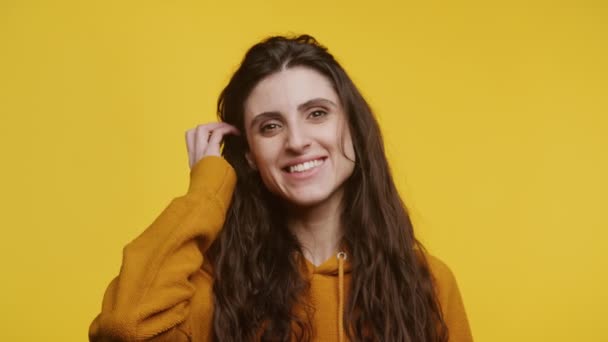 リラックスした女性が笑顔で髪に触れ マッチングバックグラウンドの黄色いセーターで陽気 — ストック動画