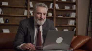 Üst düzey işadamı, bir ofis ortamında dizüstü bilgisayar üzerinde çalışırken onay veriyor.