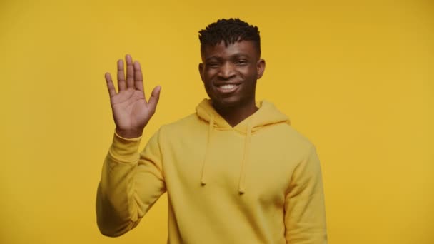 Uśmiechnięty Mężczyzna Żółtej Bluzie Podnoszący Rękę Przyjaznym Powitaniu Odizolowany Żółtym — Wideo stockowe