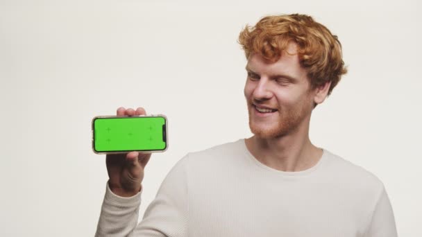 Fröhlicher Ingwermann Zeigt Ein Handy Mit Grünem Bildschirm Vor Weißem — Stockvideo