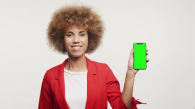 Kırmızı ceketli gülümseyen kadın yeşil ekranlı telefonu gösteriyor, beyaz ekranda izole edilmiş.