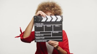 Kıvırcık saçlı kadın beyaz arka planda izole edilmiş bir film sehpası tutuyor.