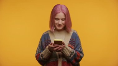 Akıllı telefondan iyi haberler okuyan neşeli kadın sarı arka planda izole edilmiş.