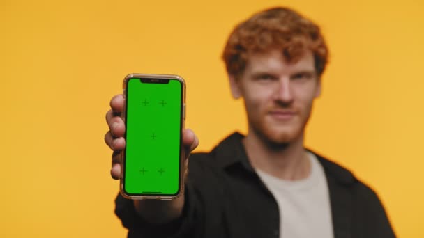 イエローバックグラウンドで隔離されたテクノロジーモックアップのための緑色の画面を持つ携帯電話を示す自信のある男 — ストック動画