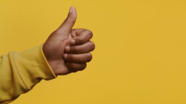 Bir adamın eli, canlı sarı bir arka plana başparmak kaldırıyor.