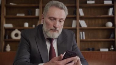 Üst düzey yönetici akıllı telefonunu dikkatli bir şekilde kullanır. Gelişmiş ofis ortamında modern iş iletişiminin dinamik doğasını yansıtır.