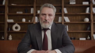 Üst düzey bir işadamının portresi kameraya bakıyor, özgüven ve otorite yayıyor, sofistike bir ofis ortamında oturuyor.