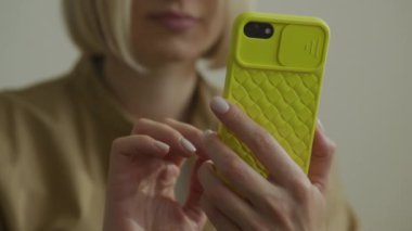Sarı desenli akıllı telefon kılıfını tutan bir kadının elleri dijital etkileşime odaklanıyor.