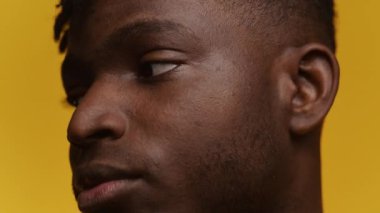 Odaklanmış bir ifadesi olan, sarı bir arkaplana dayanan genç bir Afrikalı Amerikalı 'nın huzurlu yakın plan portresi.