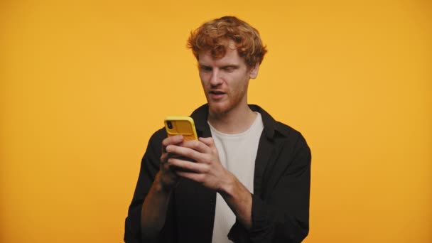 Zdenerwowany Młody Rudy Mężczyzna Pomocą Żółtego Smartfona Wyglądający Zaintrygowanego Żółtym — Wideo stockowe