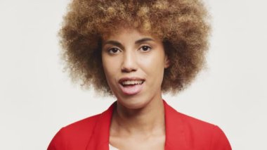Kıvırcık saçlı genç bir Afro-Amerikan kadının portresi, kendine güvenen, şık kırmızı ceketli, beyaz bir arka planda.
