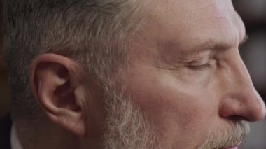 Gözlerine odaklanmış, derin düşüncelere dalmış, olgun özelliklerini ve gri sakalını vurgulayan yaşlı bir adamın yakın profil görüntüsü.