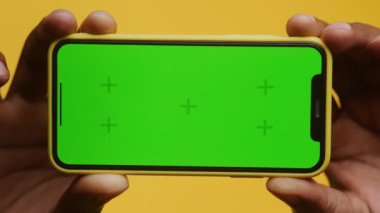 İki elle tutulan yeşil ekranlı akıllı telefonun yakın plan görüntüsünden uzaklaşın, krom anahtar bileşimi için mükemmel, canlı sarı bir arkaplan üzerine kurulmuş