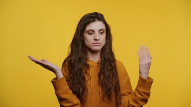 Woman with long dark hair gesturing uncertainty with both hands raised on a bright yellow background