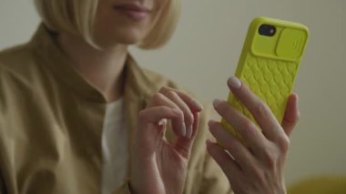 Sarı çantalı akıllı telefon kullanan kadın, el ve cihaza odaklanıyor.