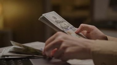 Yakın plan çekimde loş bir odada bir yığın Amerikan doları sayılıyor.