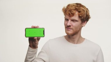 Elinde yeşil ekranlı akıllı bir telefon tutan ve beyaz arka plana karşı baş parmak kaldıran bir adam.