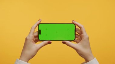 Sarı arka planda yeşil ekranlı akıllı telefonu tutan kırmızı tırnaklı kadınları yakınlaştır
