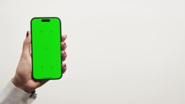 Kırmızı tırnaklı el, beyaz arka planda yeşil ekranlı akıllı telefonu tutuyor.