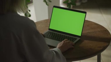 Ahşap bir masada yeşil ekran loş ışık kullanan biri.