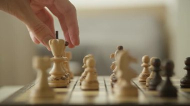 Yakın plan bir el, tahta bir satranç tahtasındaki kraliçe satranç taşını hareket ettiriyor.