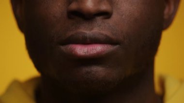 Genç adamların dudaklarını ve çenelerini sarı bir arkaplana yakın plan, dokuyu ve detayı vurguluyor.