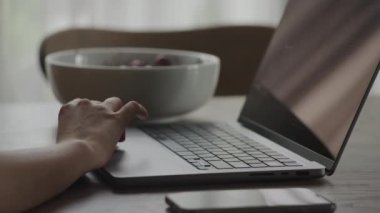 Bilgisayarında akıllı telefonu ve arka planda kasesi olan tanımlanamayan kişi kod incelemesi.